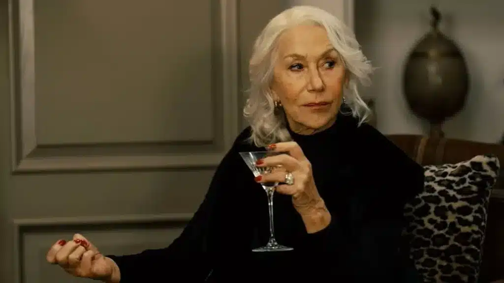 Helen Mirren amb cabell blanc llarg asseguda a una butaca amb una copa de vi a la ma